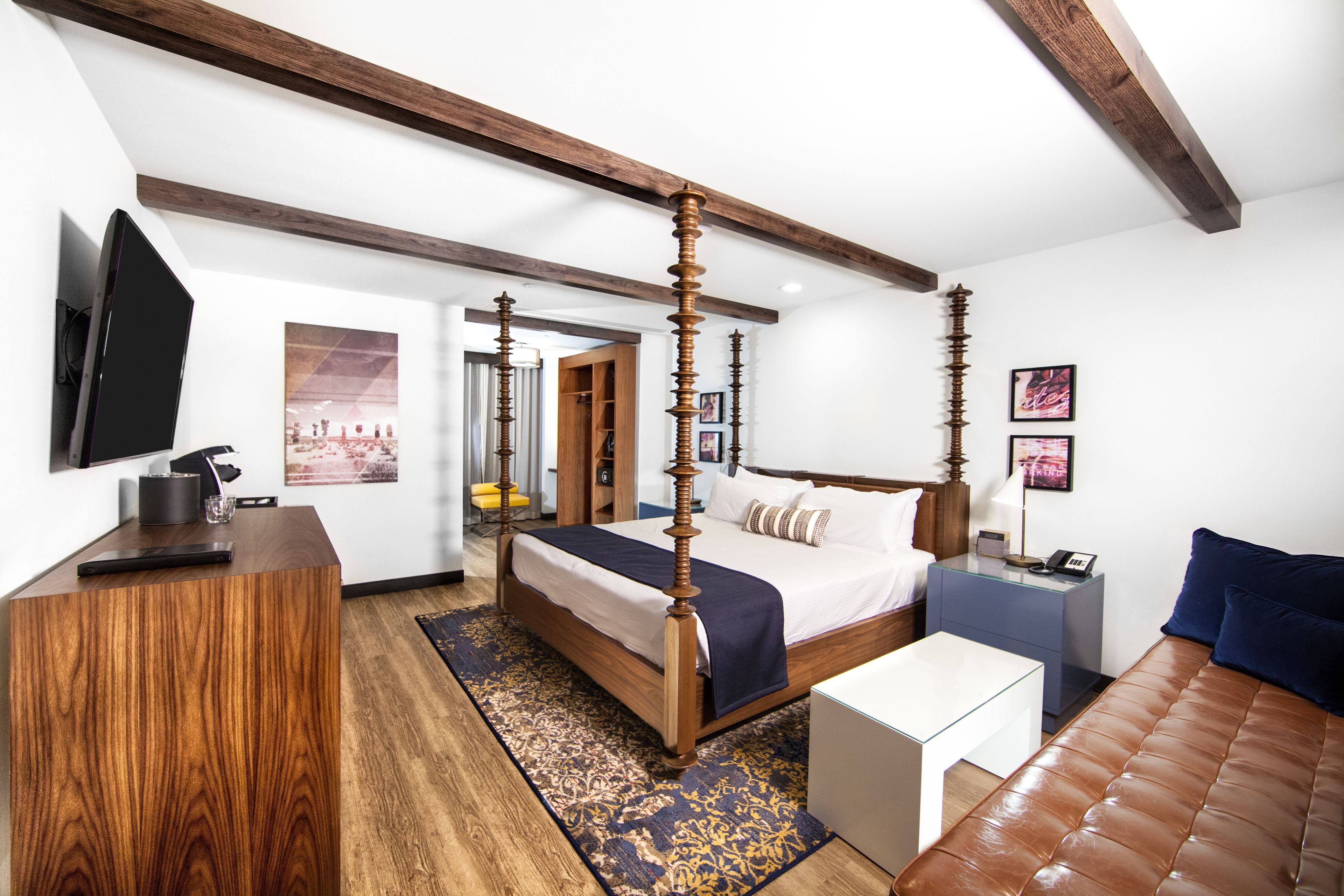 A modern bedroom with a four-poster bed, a flat-screen TV, a desk, and a leather couch.