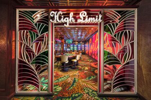 Interior vibrante de um cassino, com um aviso 'High Limit', carpete colorido e máquinas caça-níqueis.