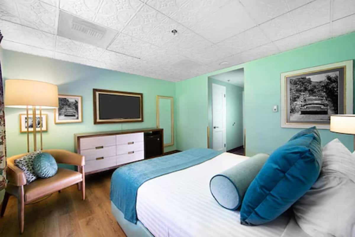 A bedroom with a bed, a desk, a chair, a dresser, and framed pictures on the wall.