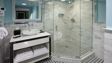 Un baño moderno con ducha de vidrio, lavamanos blanco y espejo con marco decorativo.