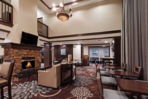 A hotel lobby with a fireplace, seating area, and a staircase. - Staybridge Suites Woodland Hills by IHG (Tulsa)