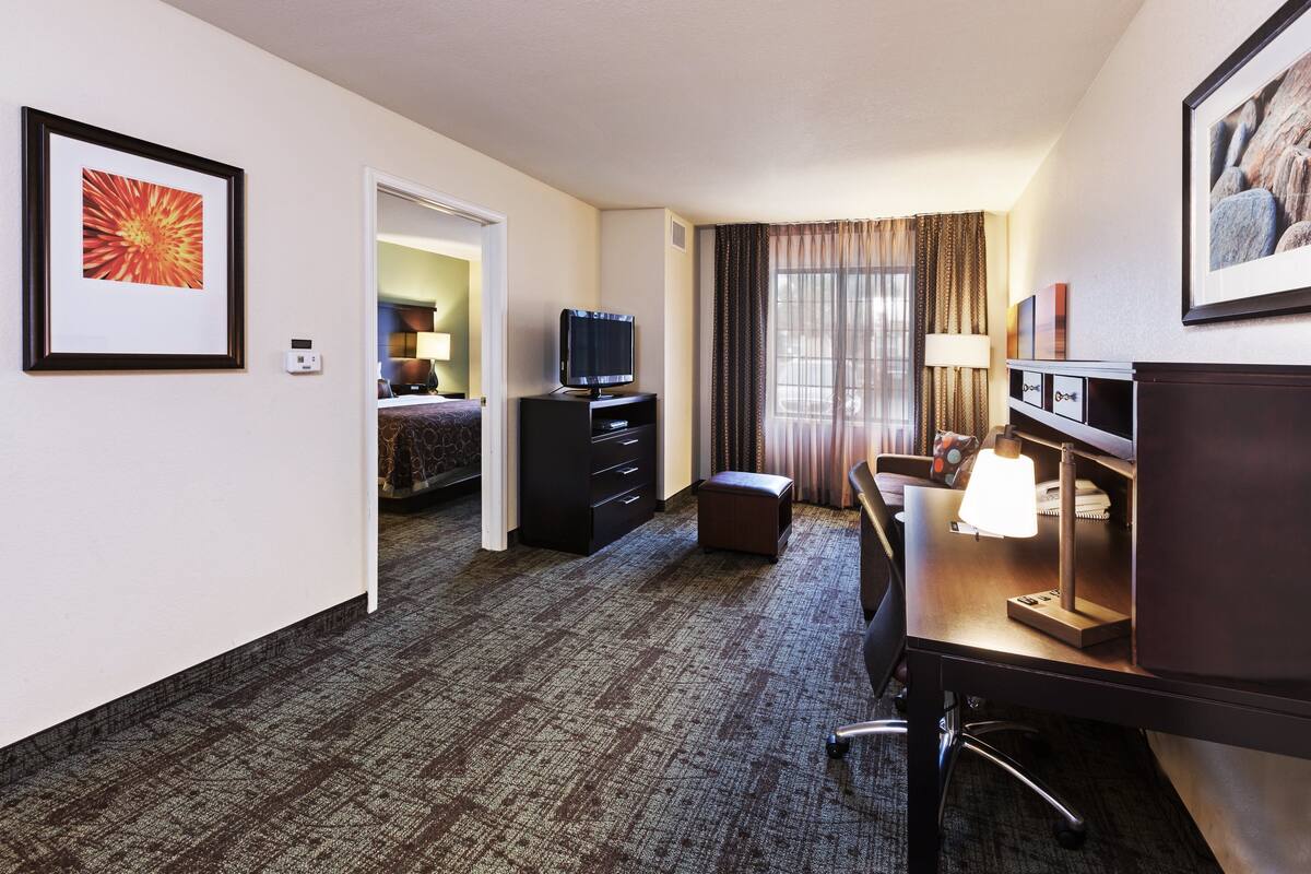 Een hotelkamer met een bed, een bureau met lamp, een televisie en een lijst aan de muur.