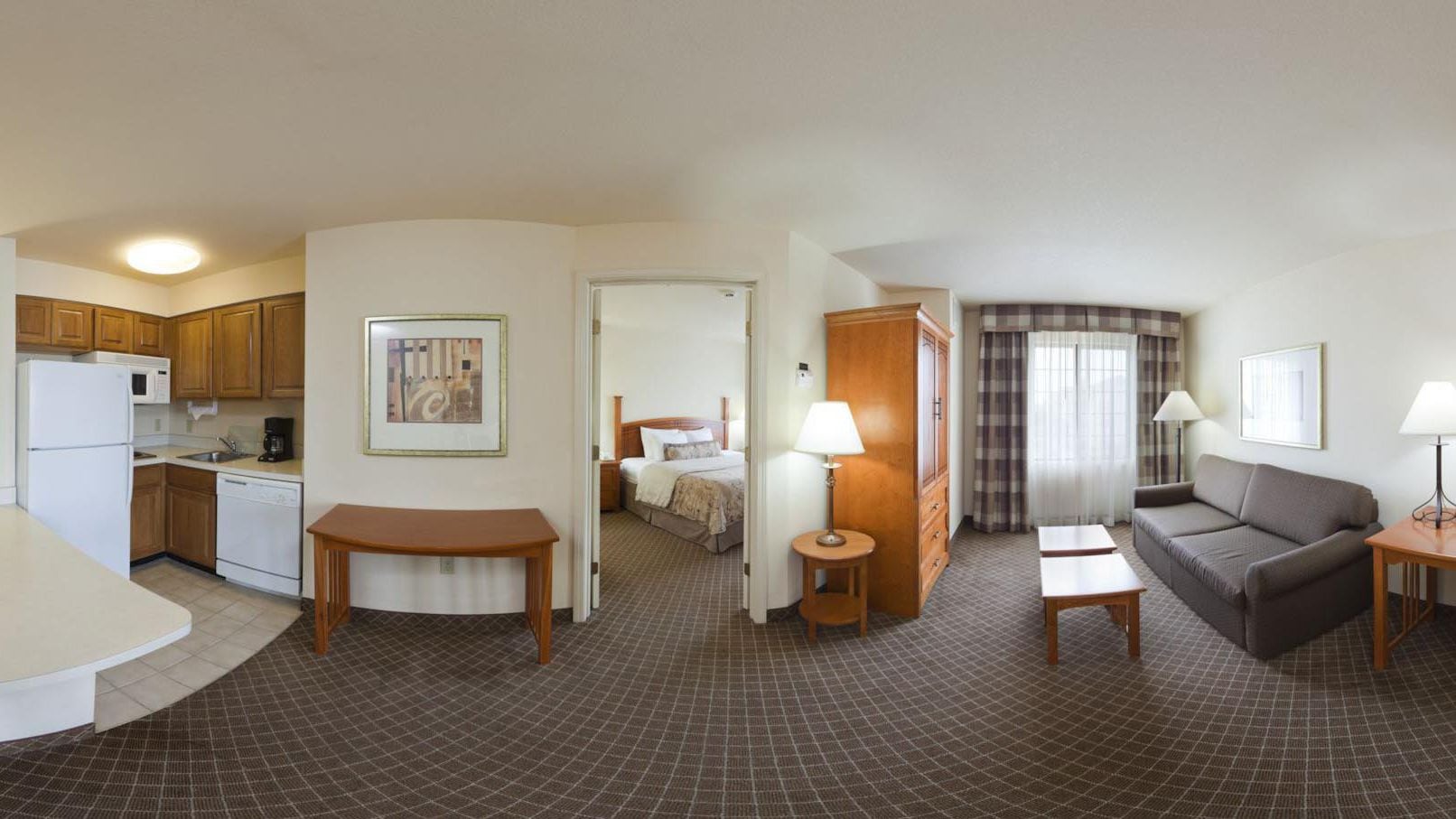 Een hotelkamer met een kitchenette, een bed, een bank, een kleine tafel en een lamp.