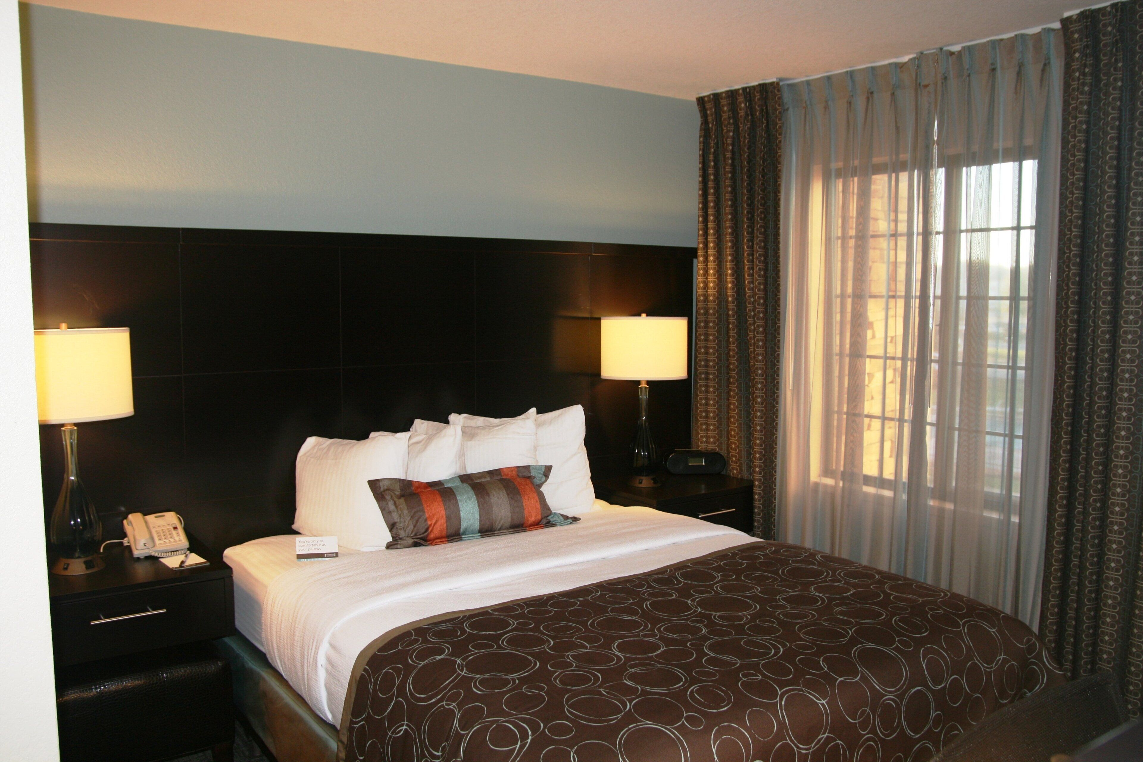 A hotel room with a large bed, two bedside lamps, a telephone, and a window with curtains.