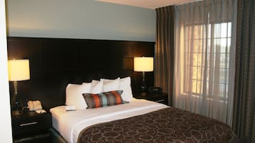 A hotel room with a large bed, two bedside lamps, a telephone, and a window with curtains.
