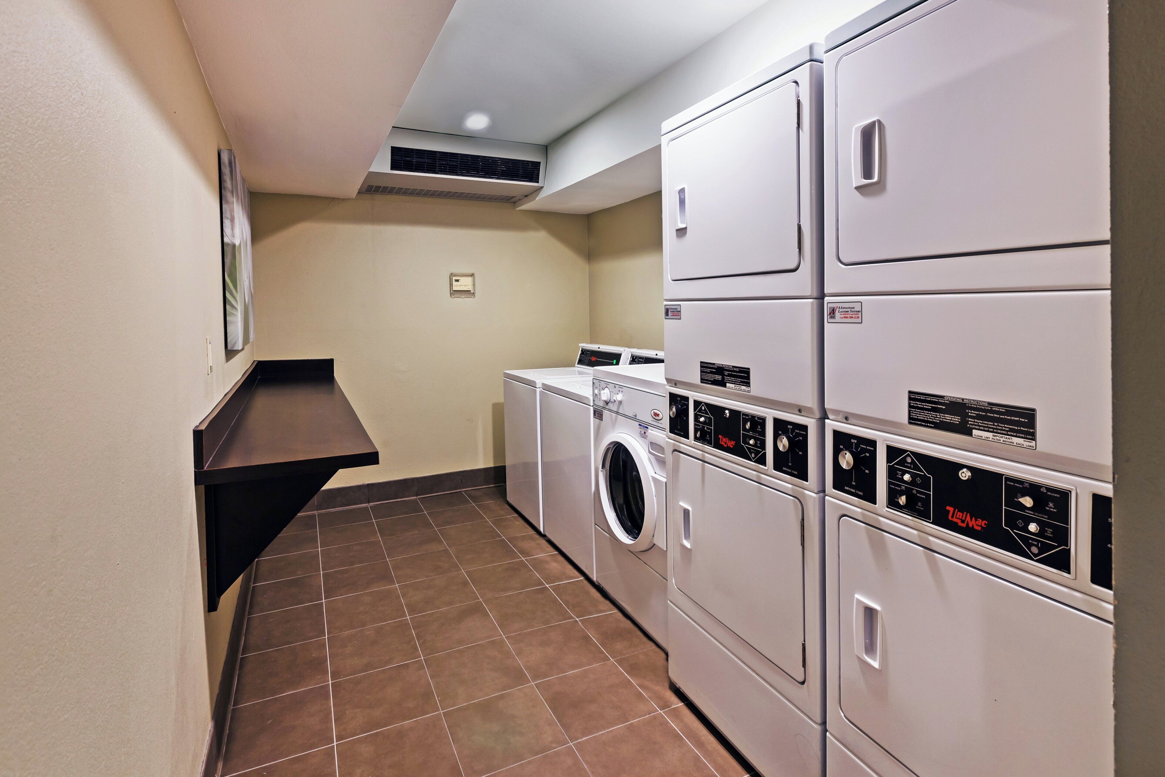 A laundry room with stacked washers and dryers, a tiled floor, and a wall-mounted vent.