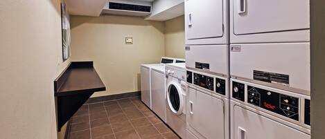 A laundry room with stacked washers and dryers, a tiled floor, and a wall-mounted vent.