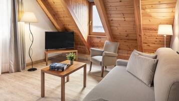 Una habitación acogedora con techo de madera, televisor de pantalla plana, un sofá, una silla y una pequeña mesa con una planta.