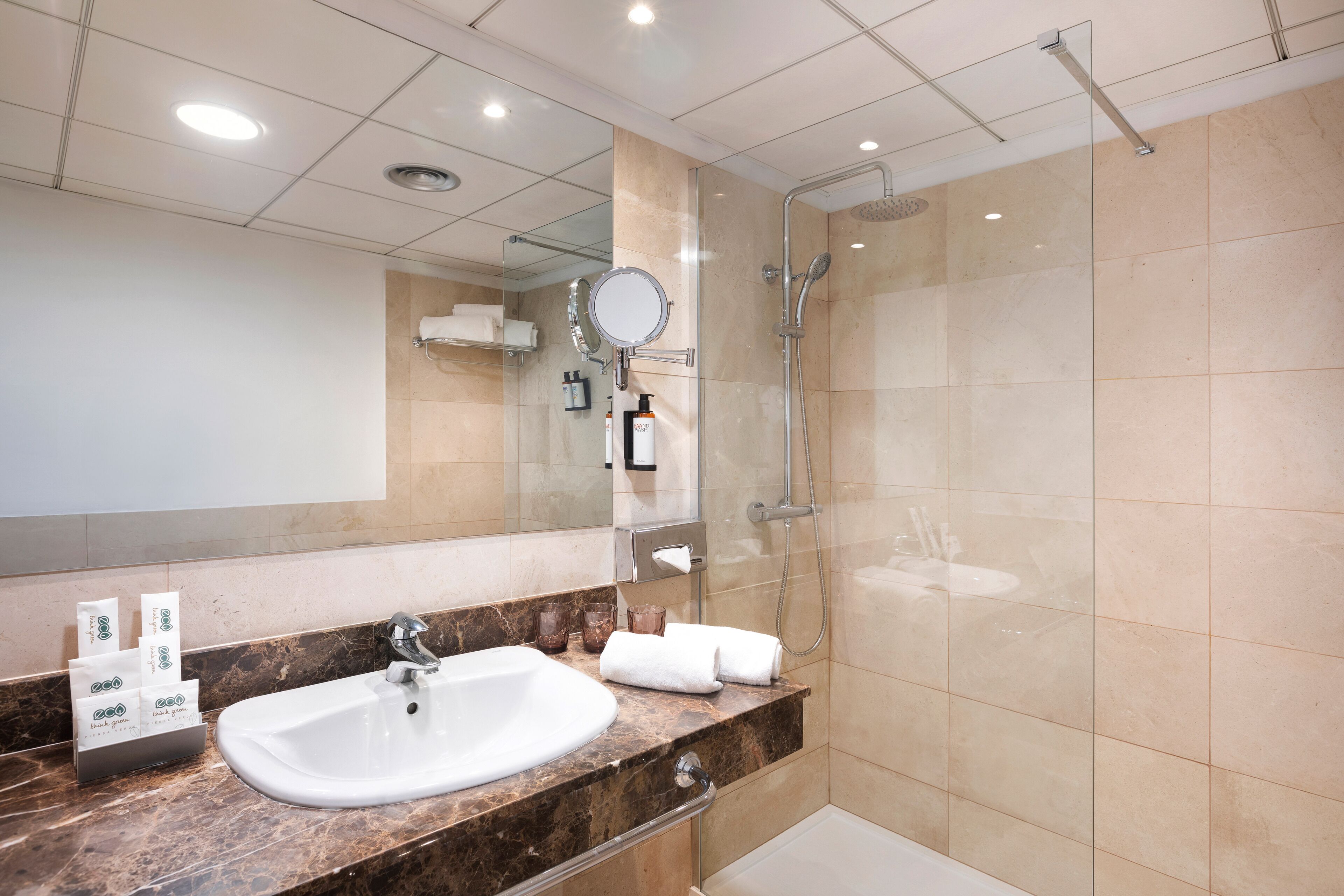 A modern bathroom with a marble sink, a large mirror, a handheld showerhead, and a glass-enclosed shower.