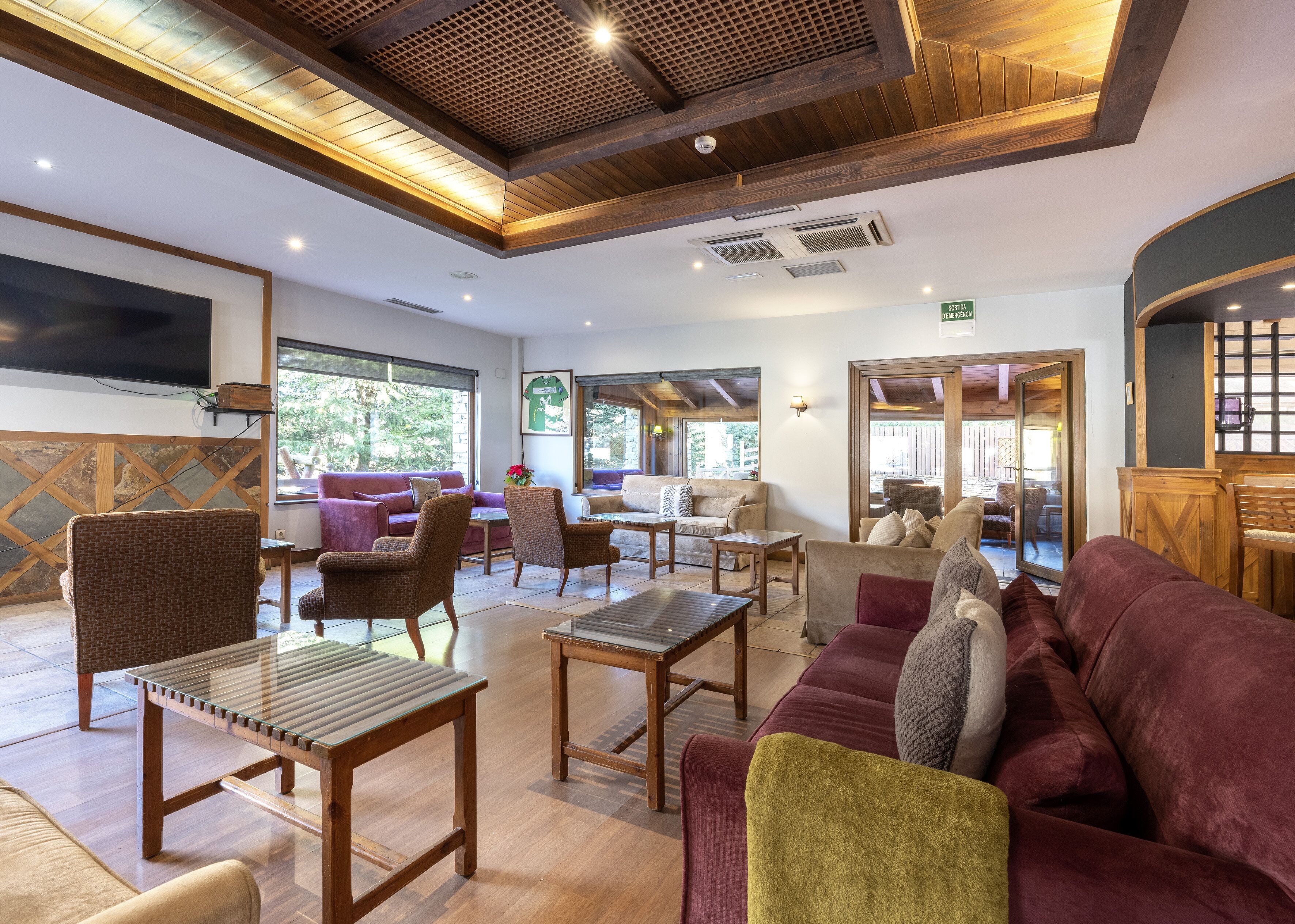 A spacious lobby with wooden ceiling beams, comfortable seating, and large windows offering views of the outdoors.