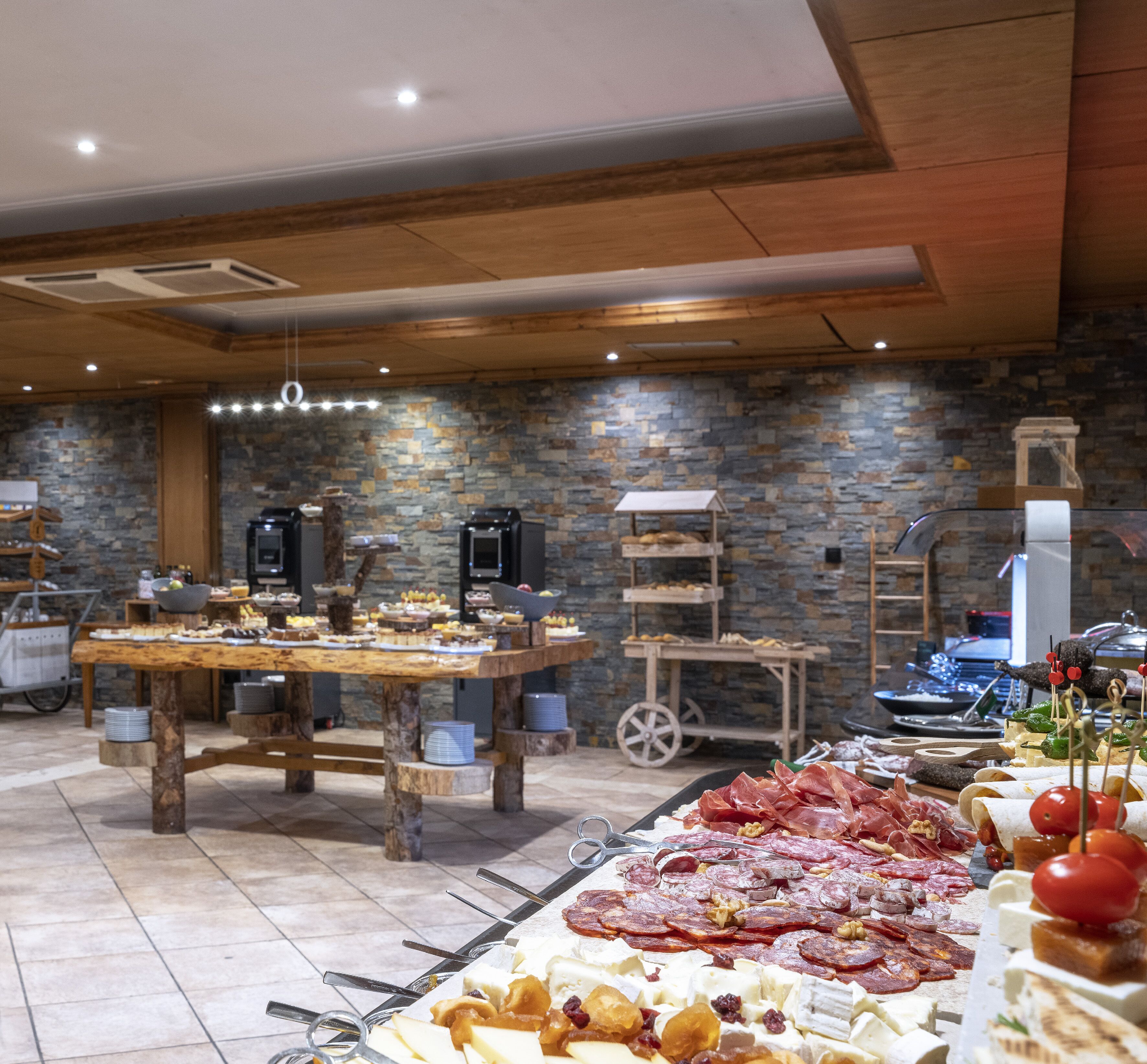 A buffet setup with a variety of food items, a stone wall background, and a wooden ceiling.