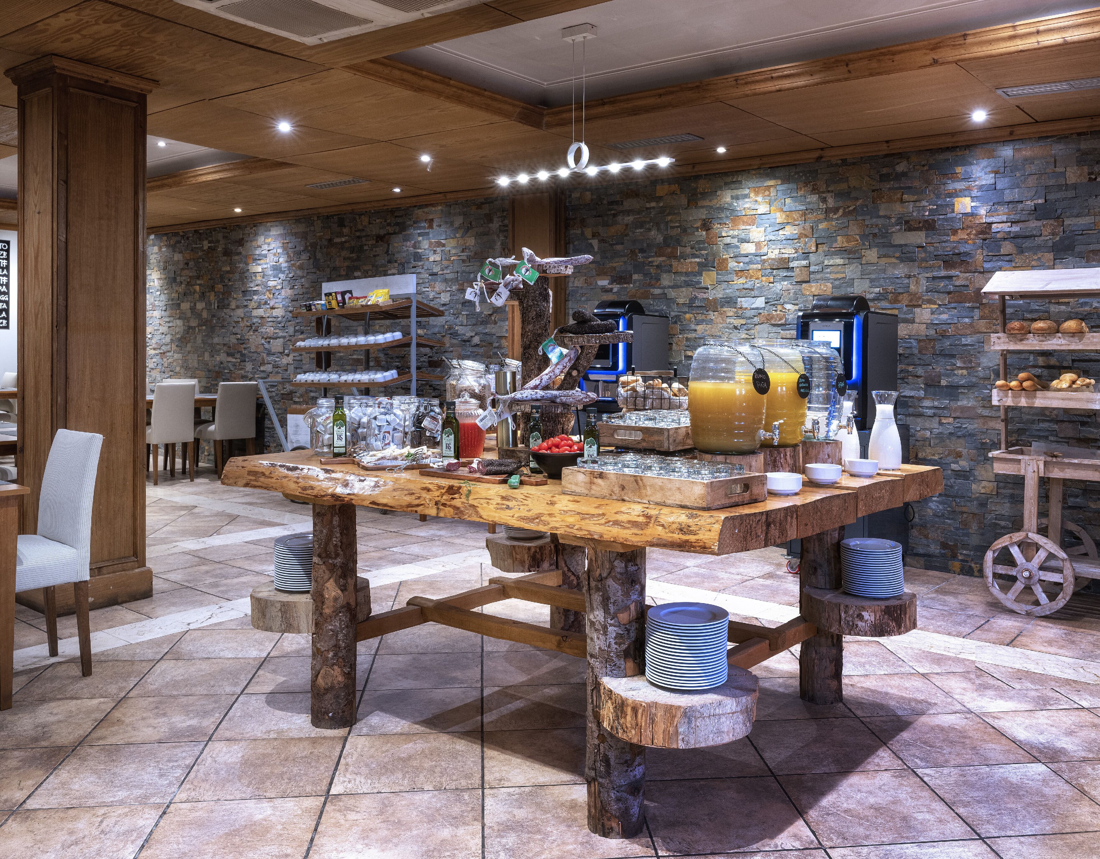 Un comedor rústico con una mesa de madera preparada para el desayuno, rodeado de paredes de piedra y vigas de madera.