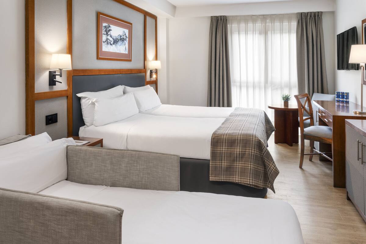 A hotel room with two beds, a desk, a chair, and a television.