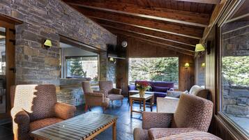 A cozy interior with stone walls, wooden beams, and a mix of wicker and cushioned furniture.