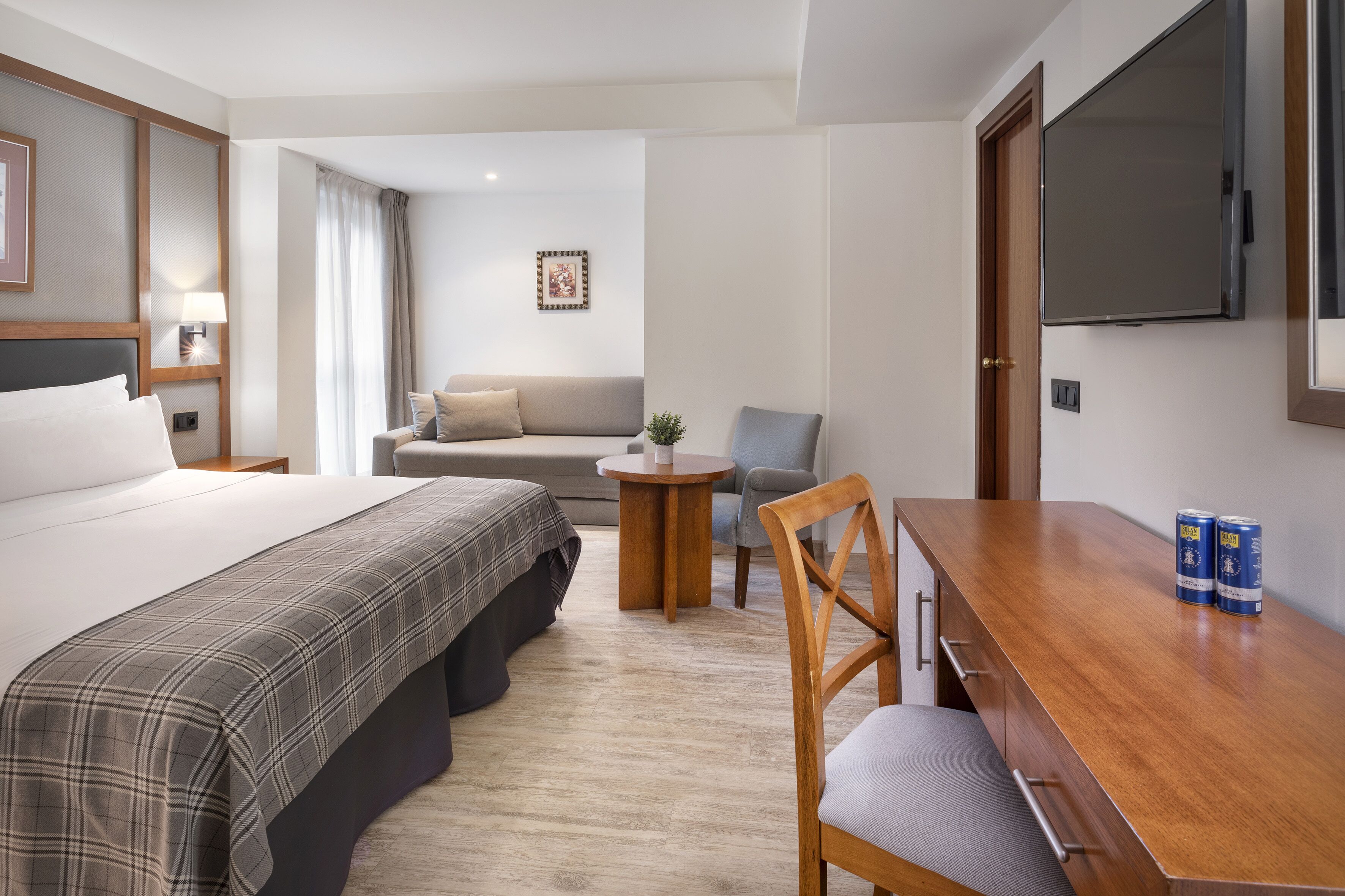 Habitación de hotel con cama, sofá, mesita redonda, silla y televisor en la pared.