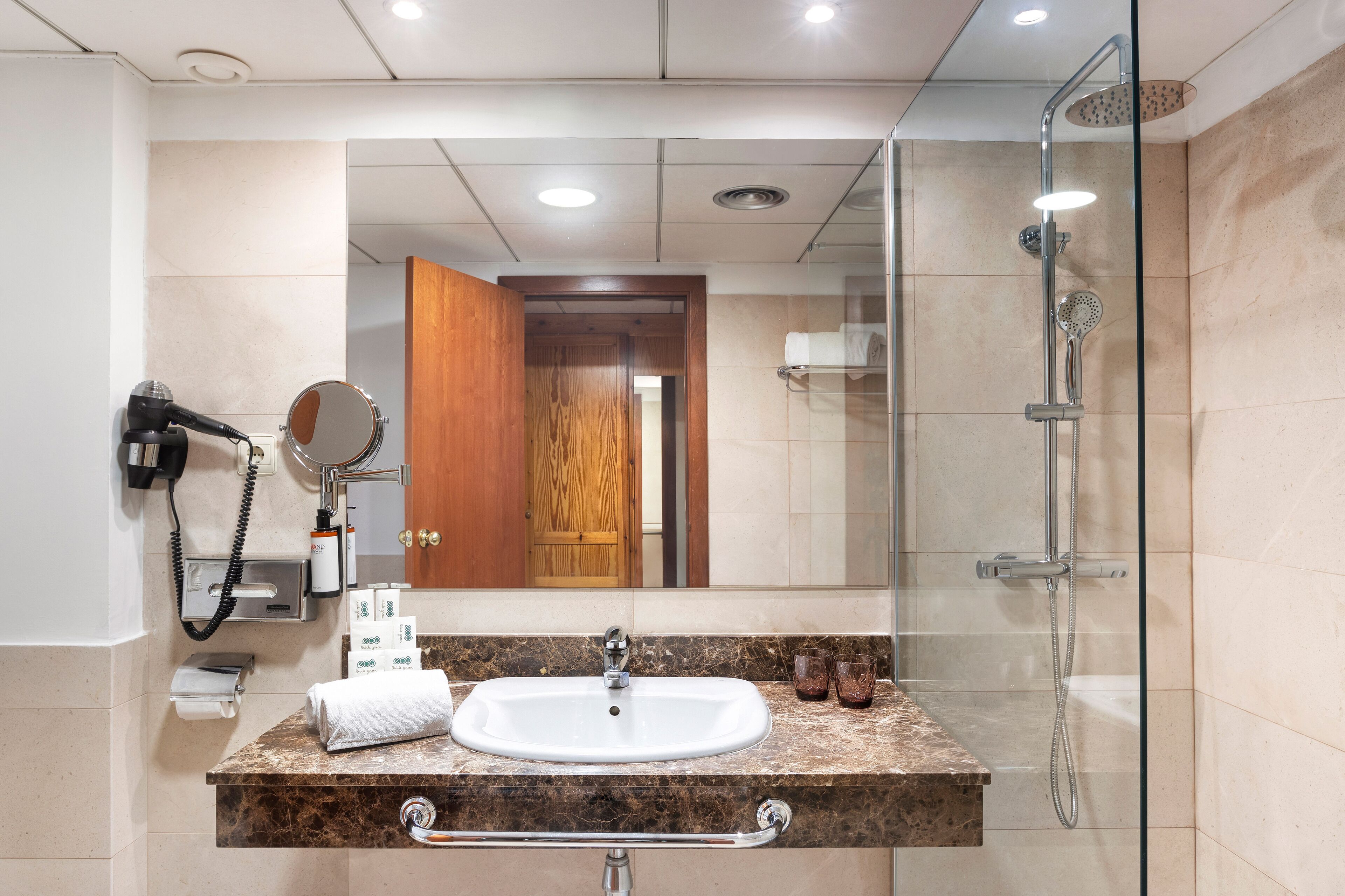 Un baño con lavamanos de mármol, cabina de ducha de vidrio, puerta de madera y espejo.