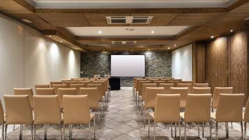A conference room with rows of chairs, a projector screen, and a stone wall.