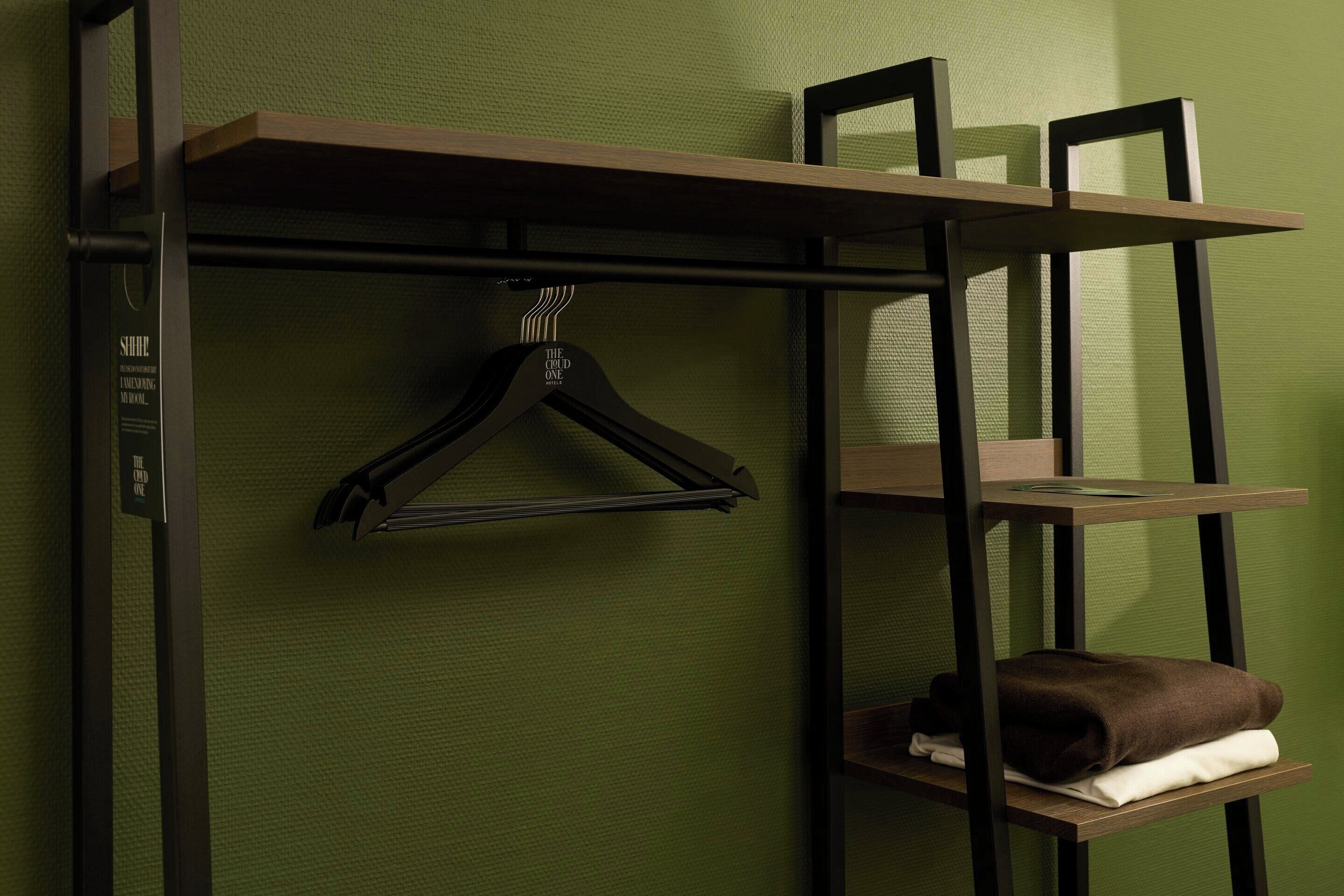 A room with a green textured wall, a black metal shelf unit with a brown towel and a black hanger, and a framed picture on the top shelf.
