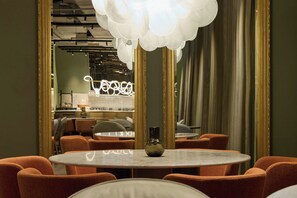 A dining area with round tables, orange chairs, a vase on the table, and a large mirror with a gold frame. - The Cloud One Frankfurt-Metropolitan (Frankfurt)