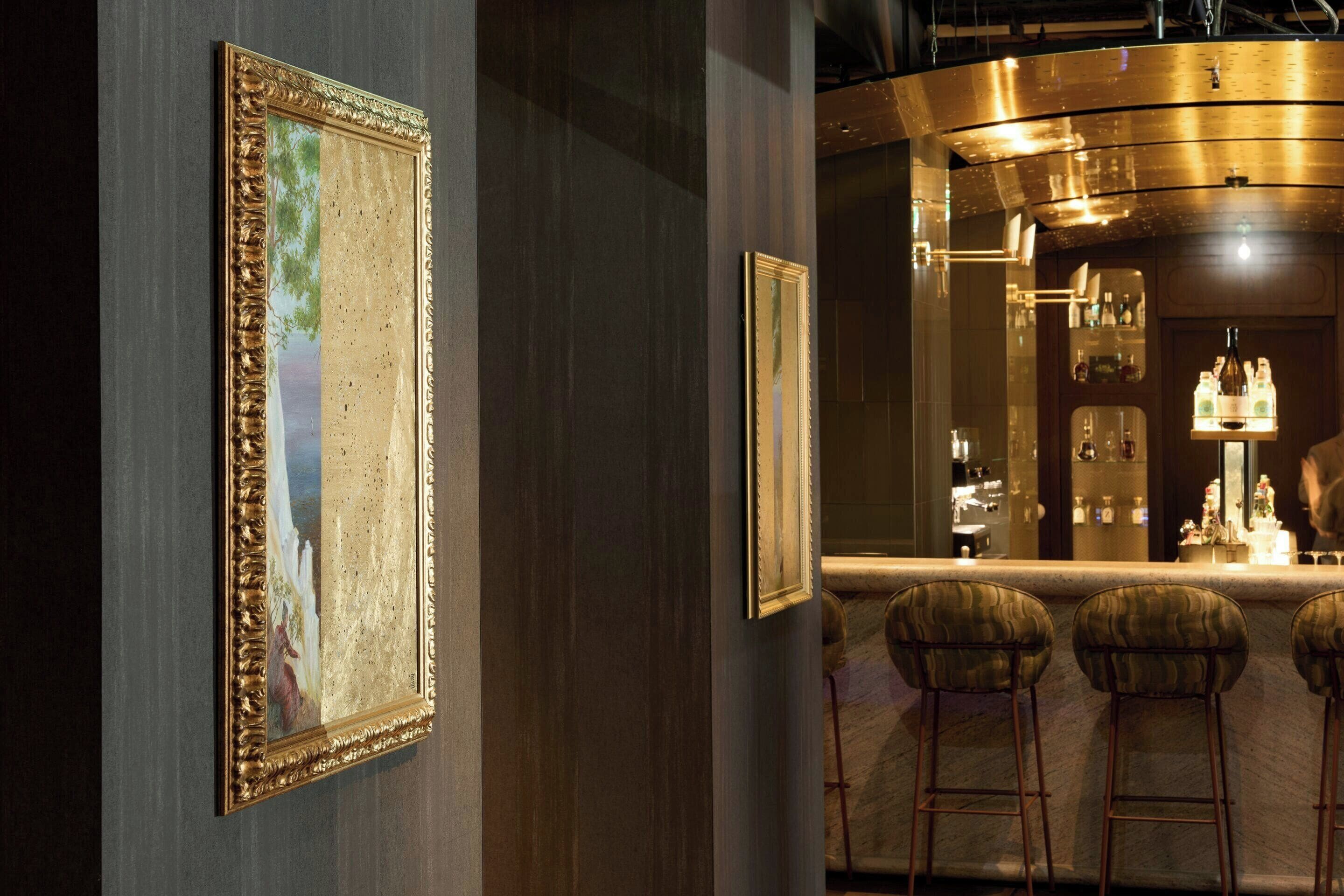 A bar area with a counter, stools, and framed artwork on the wall.