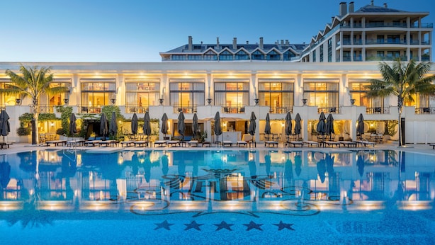 A hotel with a large pool, outdoor seating, and a well-lit facade.