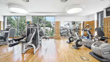 Un gimnasio moderno con diversas máquinas de ejercicio, ventanas amplias y piso de madera.