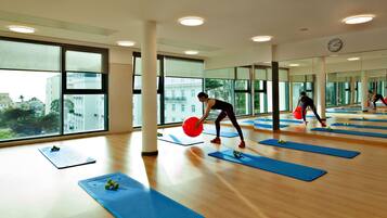 Un gimnasio amplio con ventanas grandes, piso de madera y colchonetas de ejercicio.