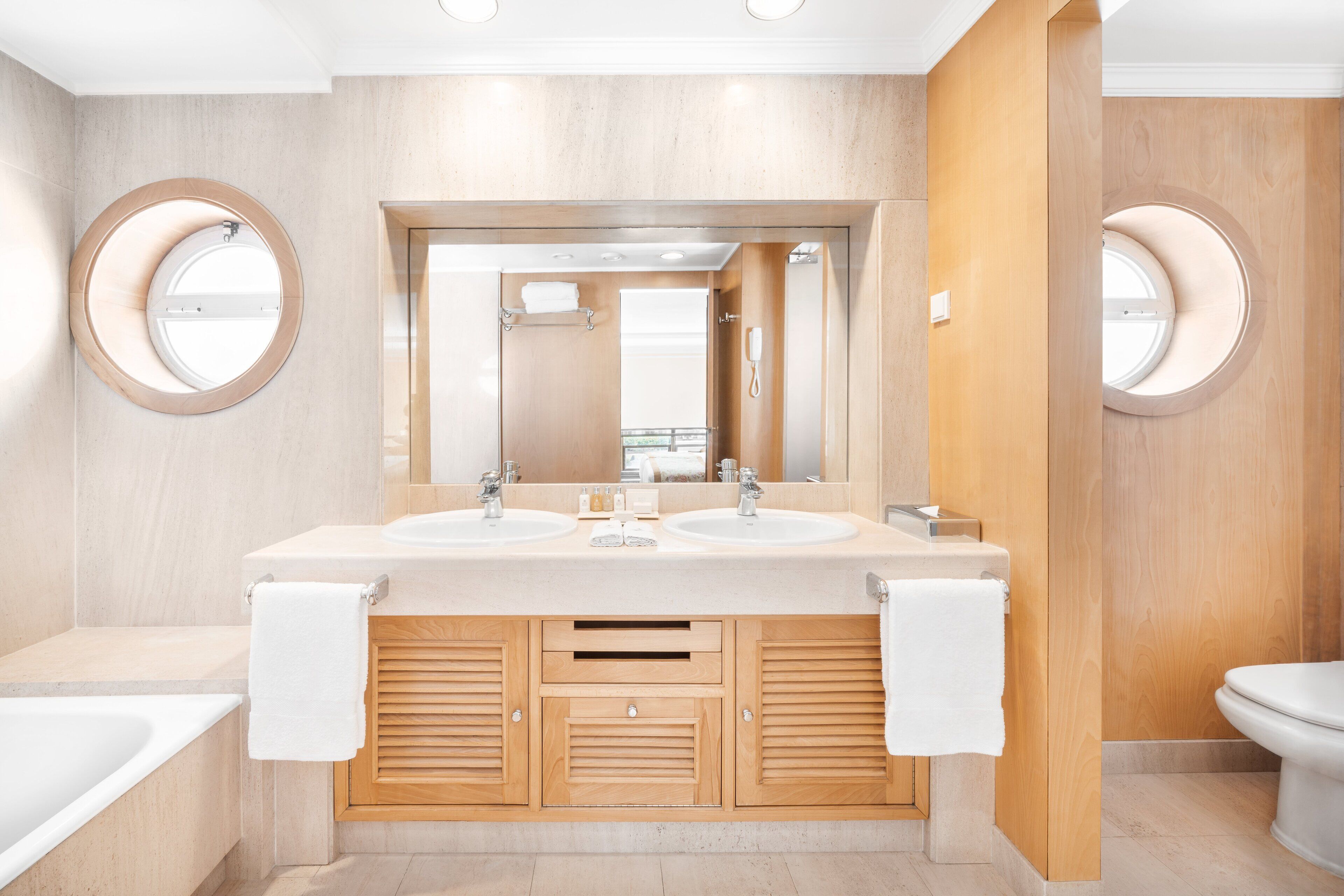 Un baño moderno con dos lavamanos, un espejo grande, armarios de madera y un inodoro.