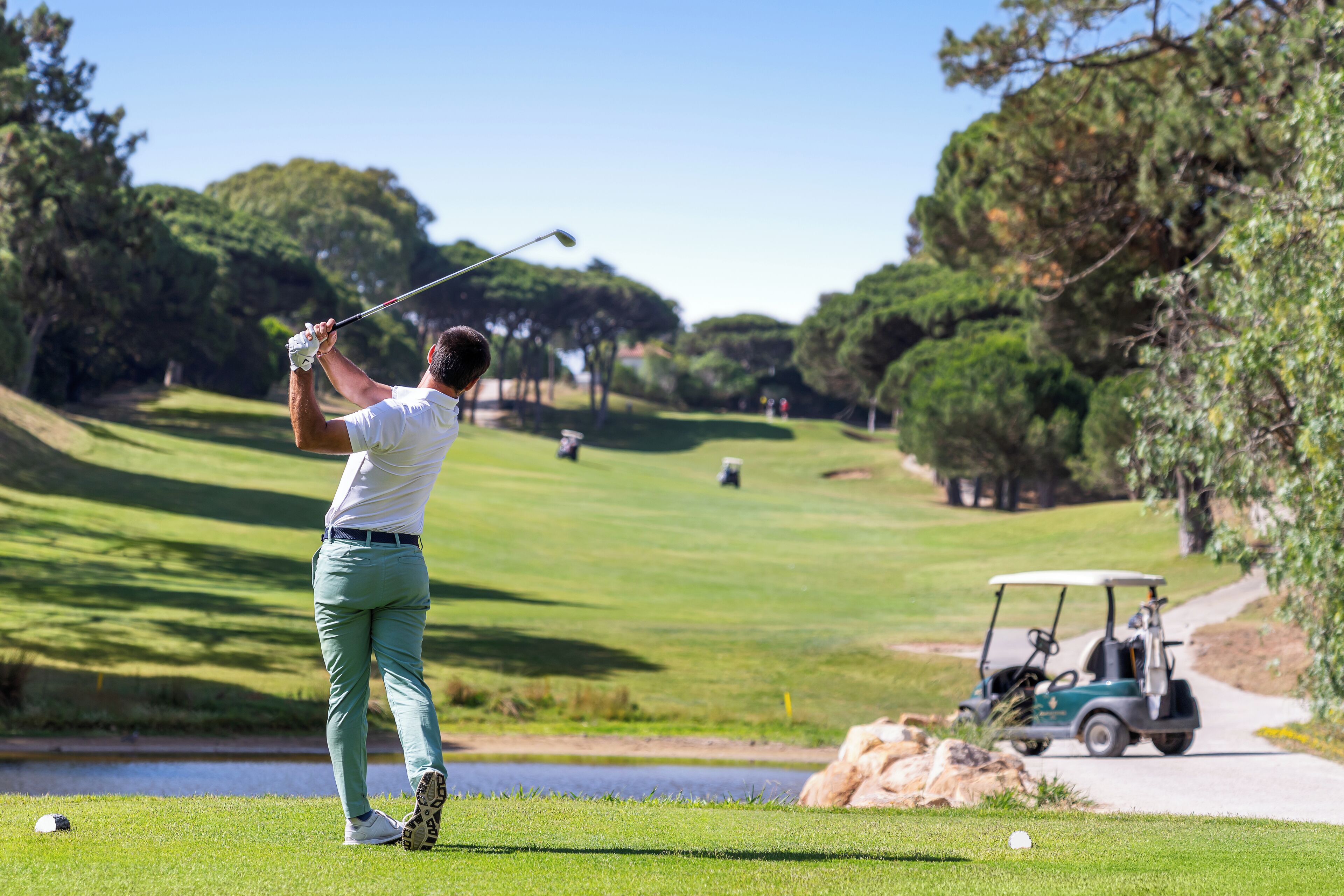 Un golfista en un campo de golf, con un carrito de golfe al fondo.
