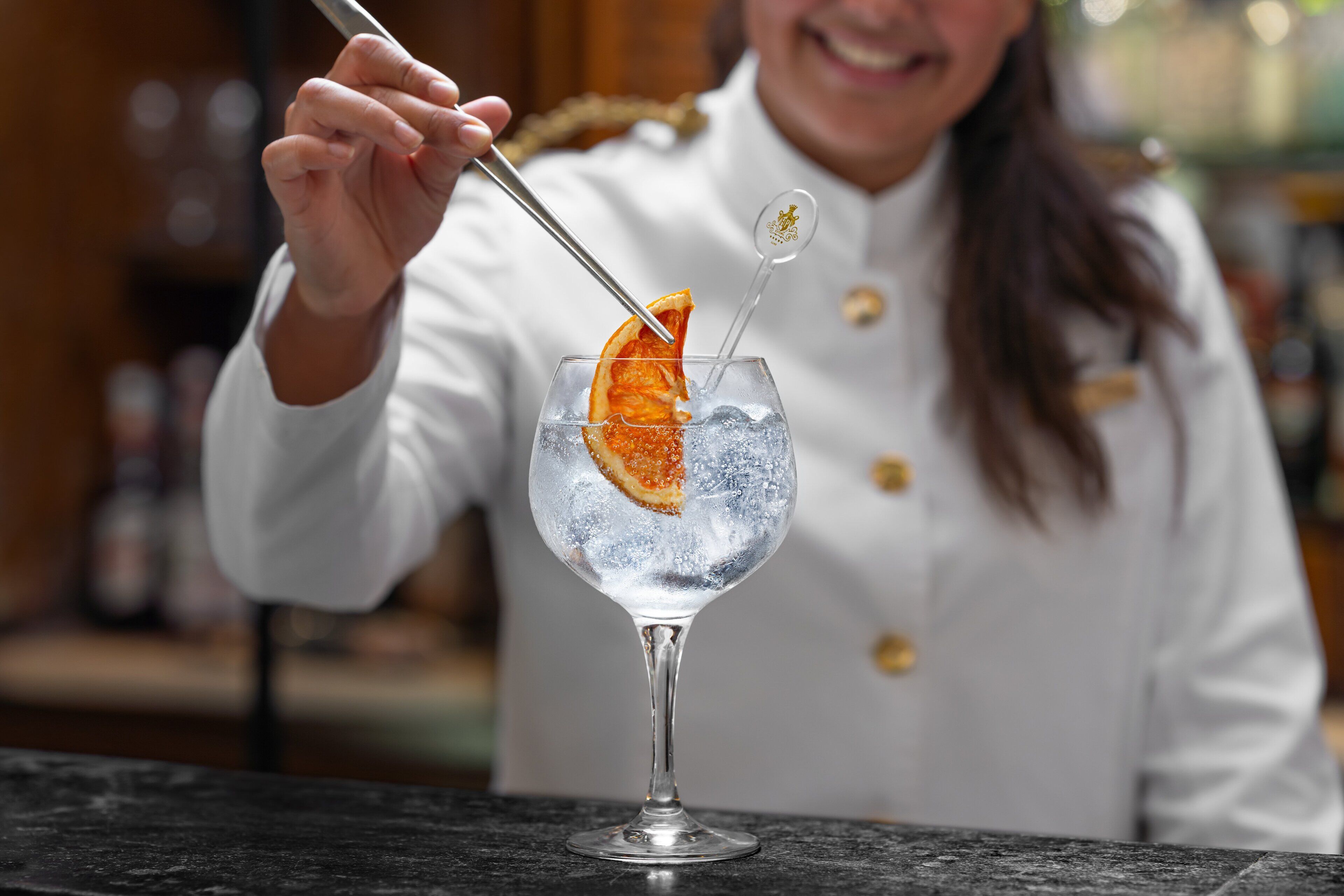 A bartender preparing a cocktail with an orange slice garnish.
