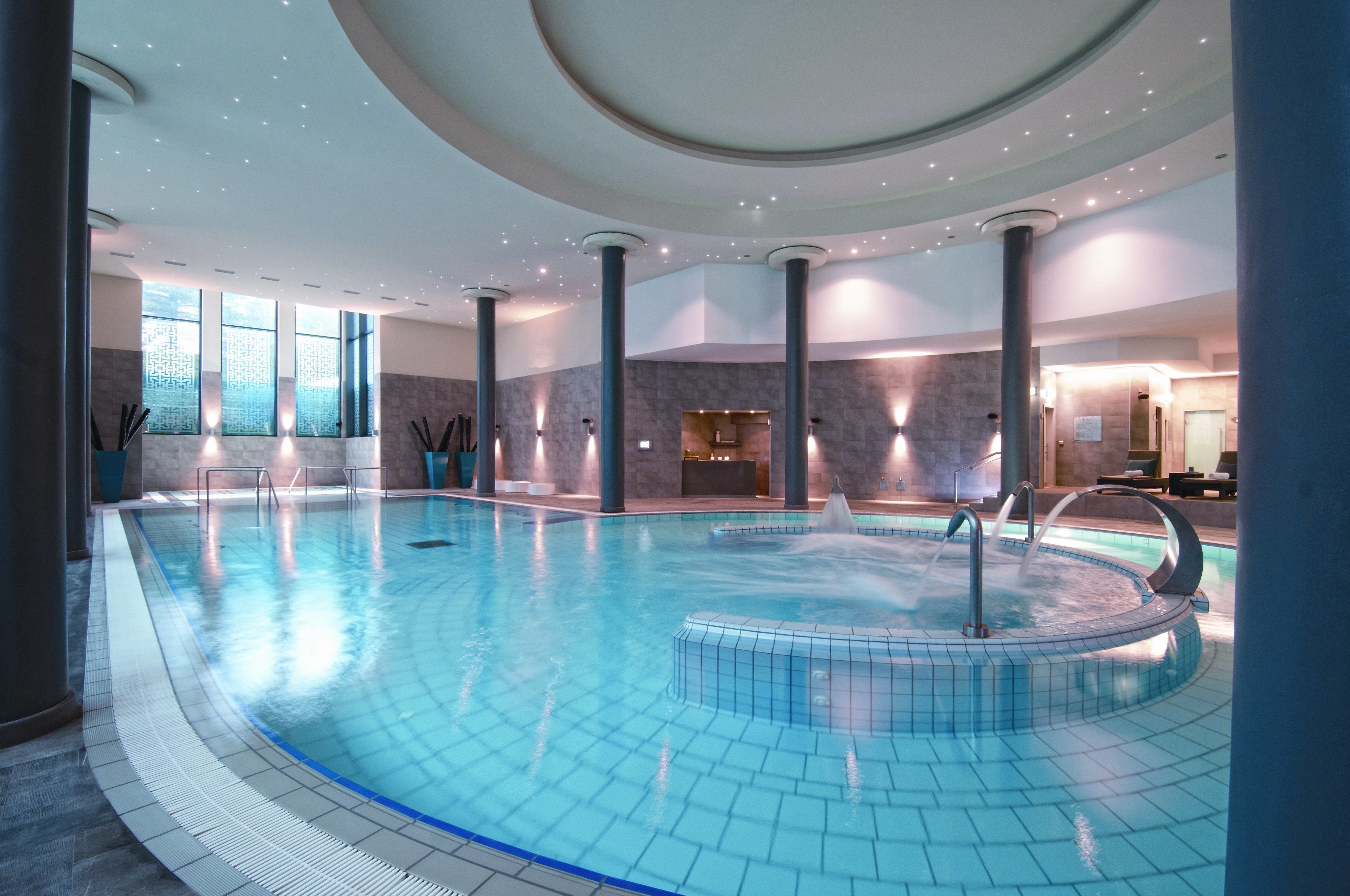 Une piscine intérieure dotée d’un jacuzzi circulaire, entourée de colonnes et recouverte d’un sol carrelé.