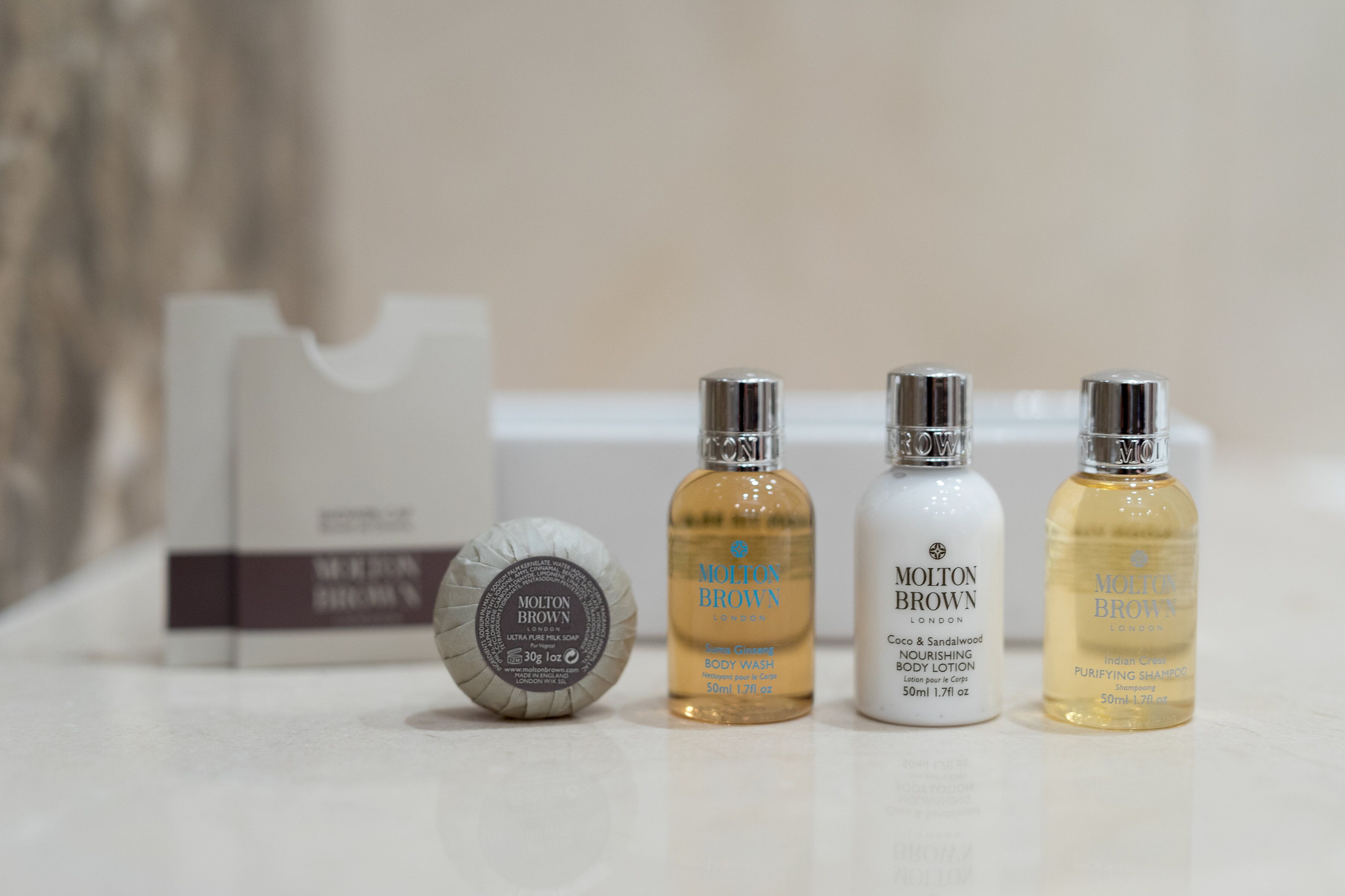 Three bottles of Molton Brown body wash and a bar of soap on a white surface.