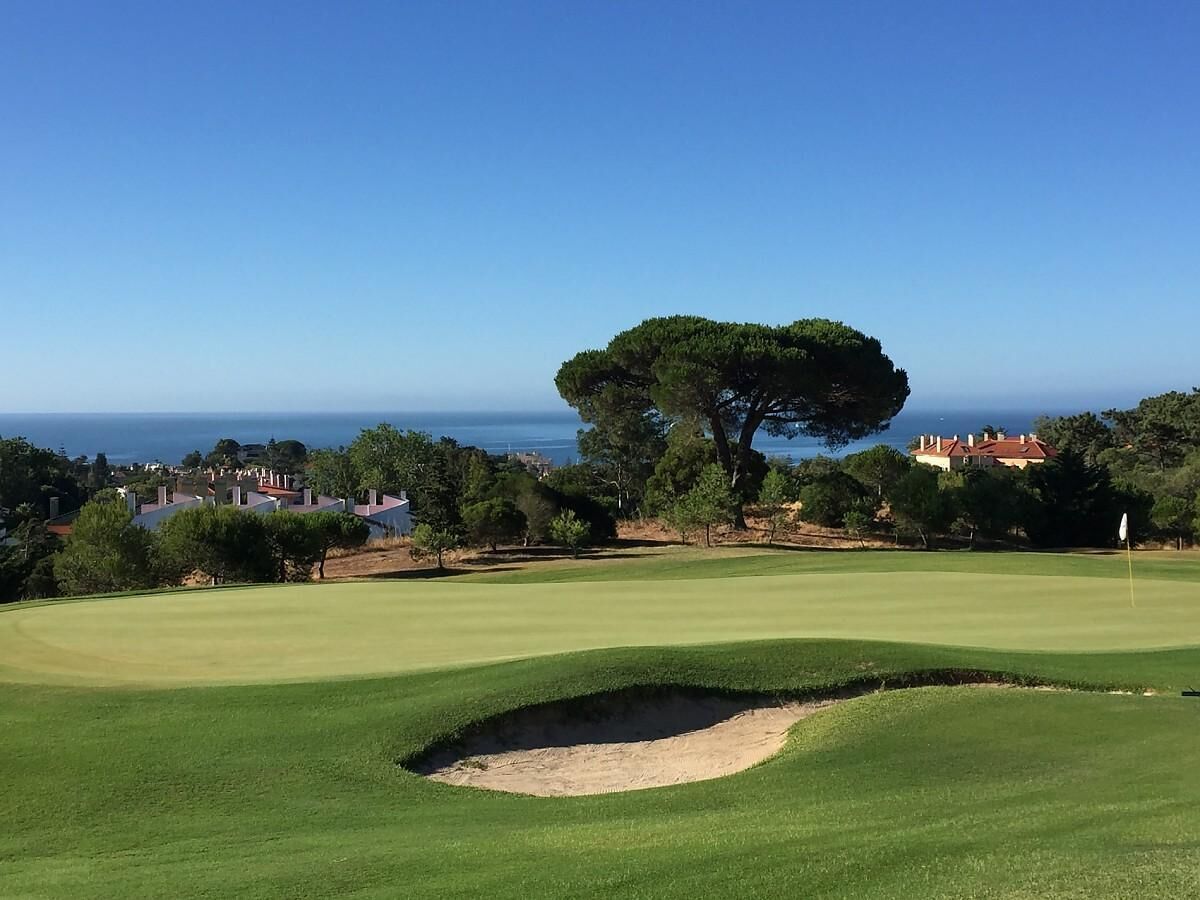 A golf course with a clear view of the ocean and residential buildings in the background.