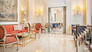 A spacious lobby with a red sofa, matching armchairs, a glass coffee table, and a chandelier.