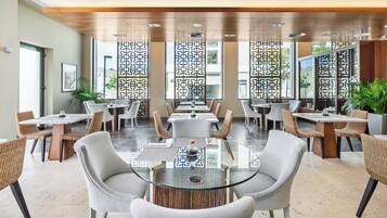 A modern dining area with glass-top tables, wicker chairs, and decorative panels.