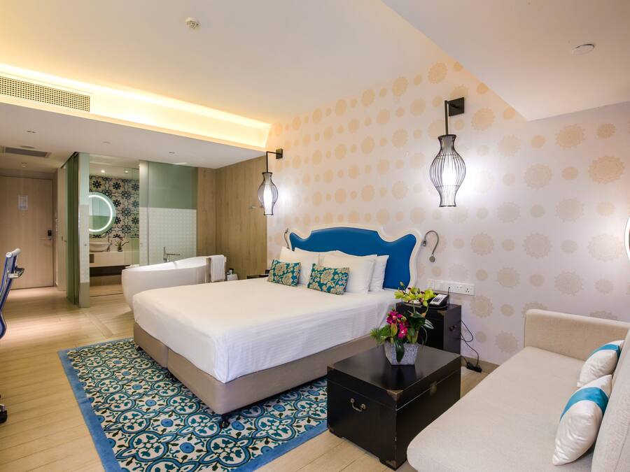 A modern hotel room with a large bed, a sofa, a desk, and a bathroom visible through an open door.