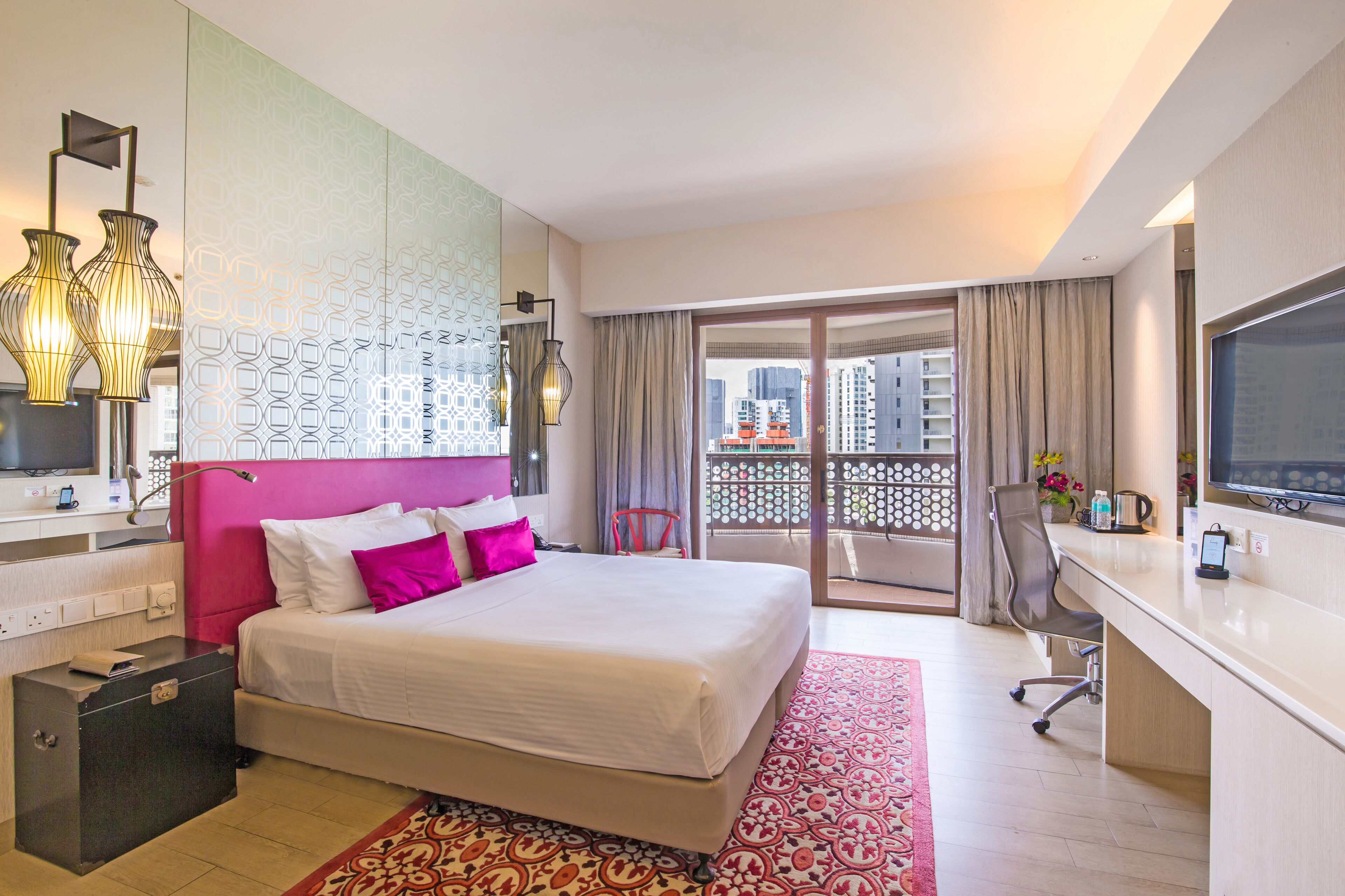 A hotel room with a bed, a desk, a TV, a bathroom, and a balcony with a view of buildings.