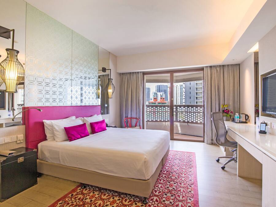 A hotel room with a bed, a desk, a TV, a bathroom, and a balcony with a view of buildings.