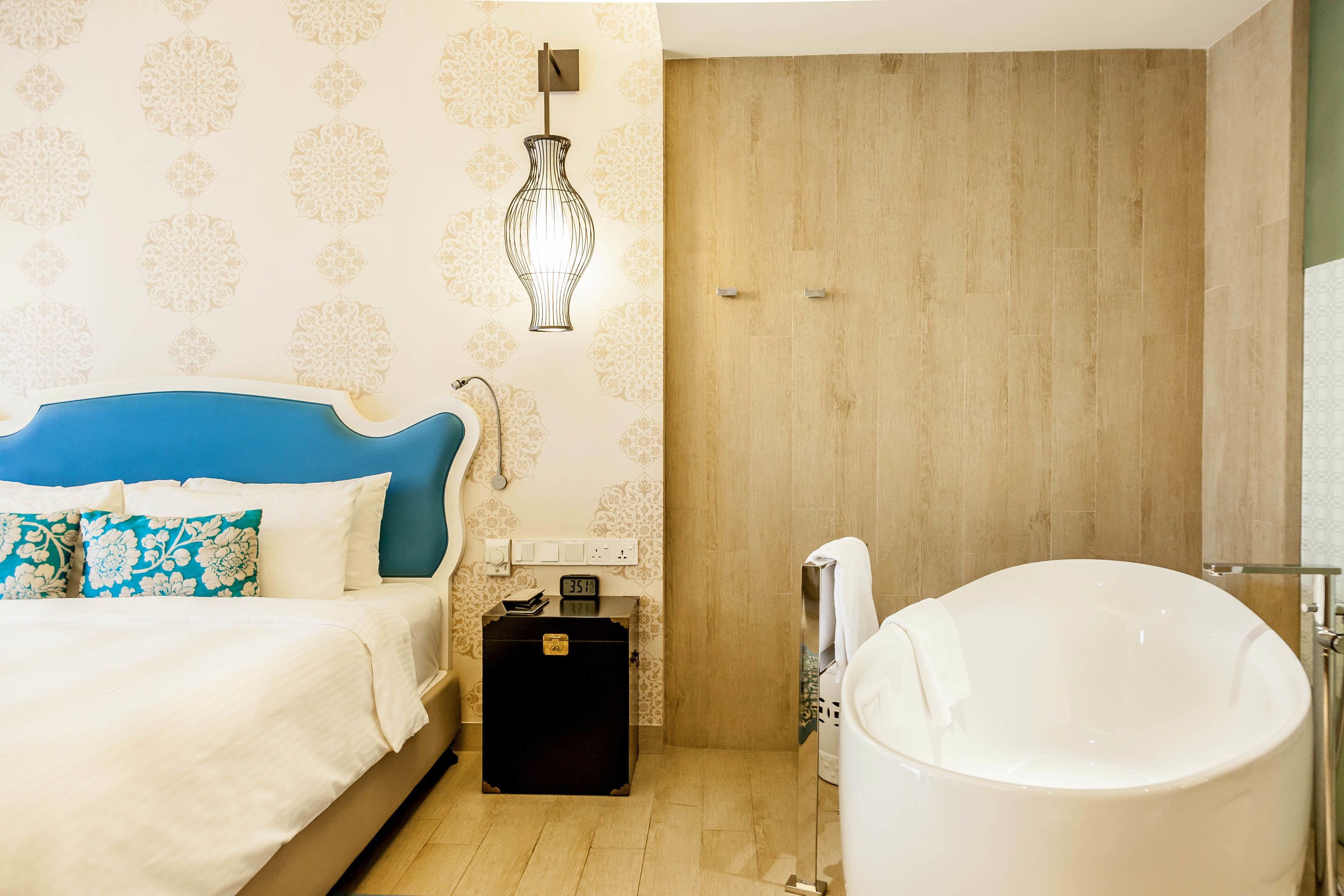 A bedroom with a bed, a nightstand, a black suitcase, a wall clock, and a large bathtub.