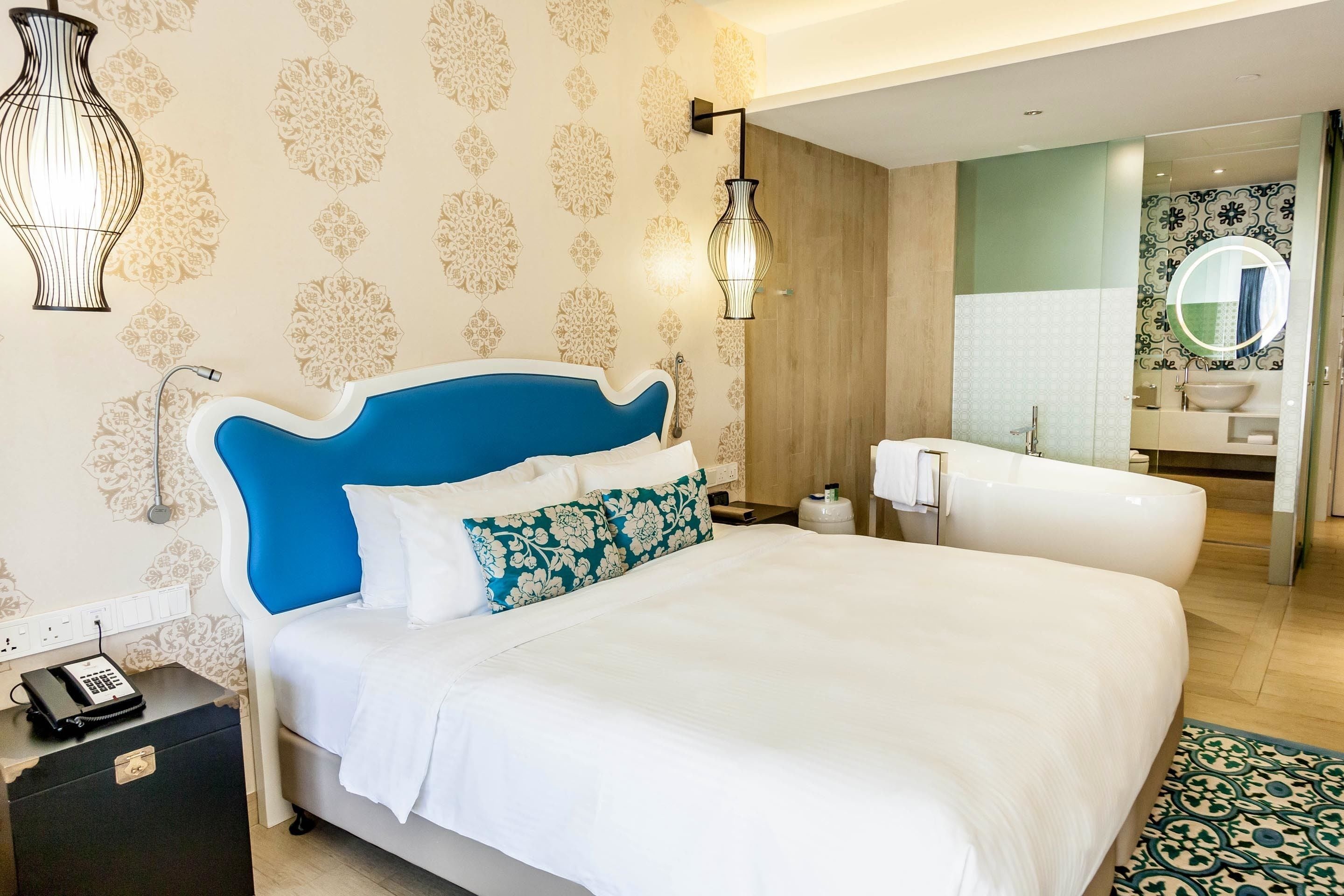 Habitación de hotel con una cama grande, una mesita de noche con teléfono, un tocador y un baño con bañera y espejo.
