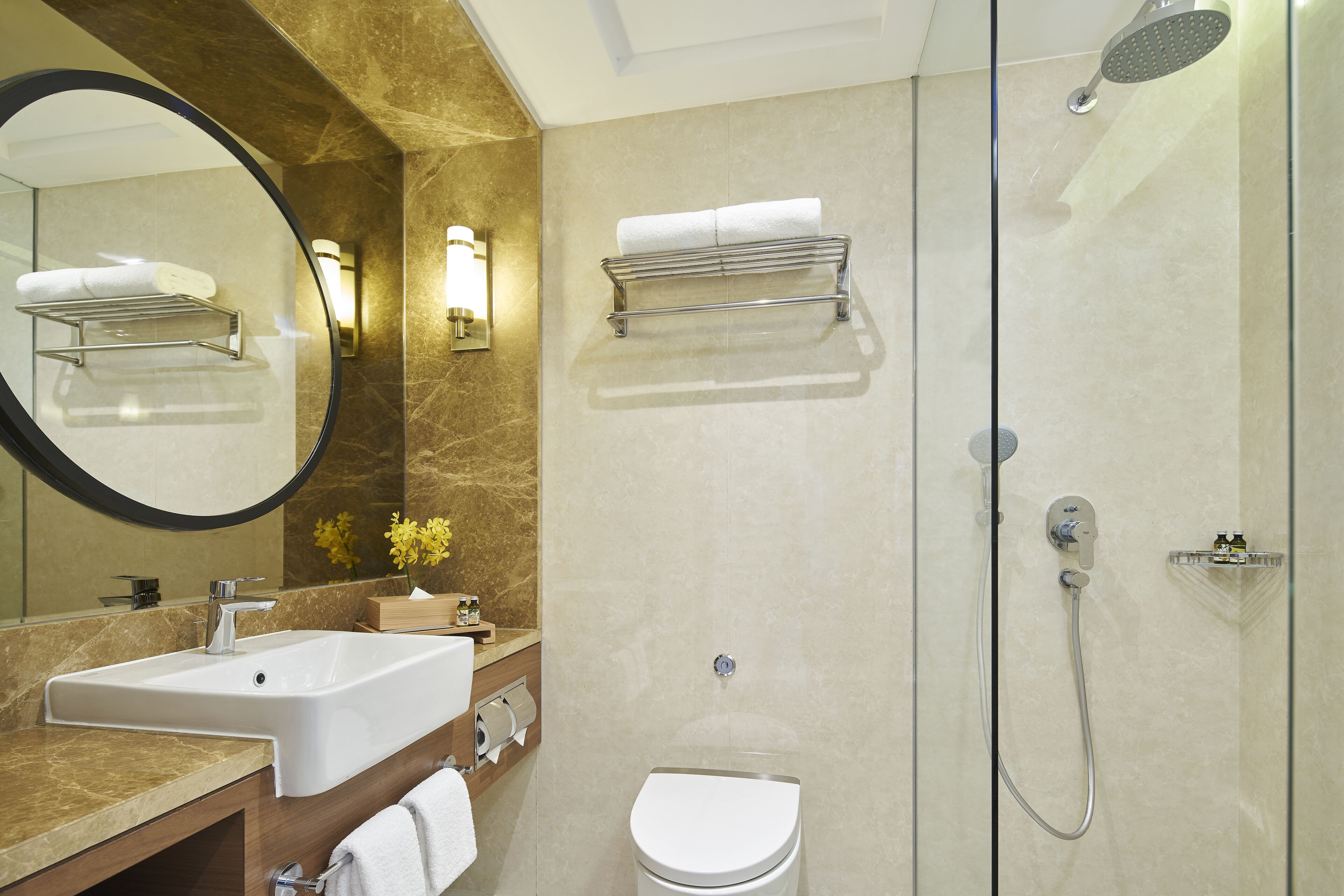 Un baño moderno con tocador de mármol, inodoro, ducha con mampara de vidrio y un espejo grande.