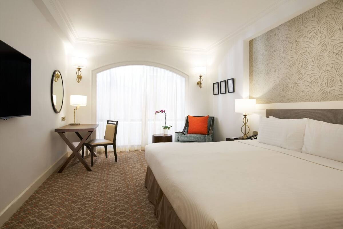 Une chambre d’hôtel avec un grand lit, un bureau avec une chaise, une télévision et une fenêtre avec des rideaux.