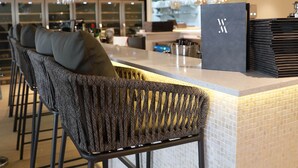 Een bar met hoge krukken, een toog en planken met flessen en glazen.
