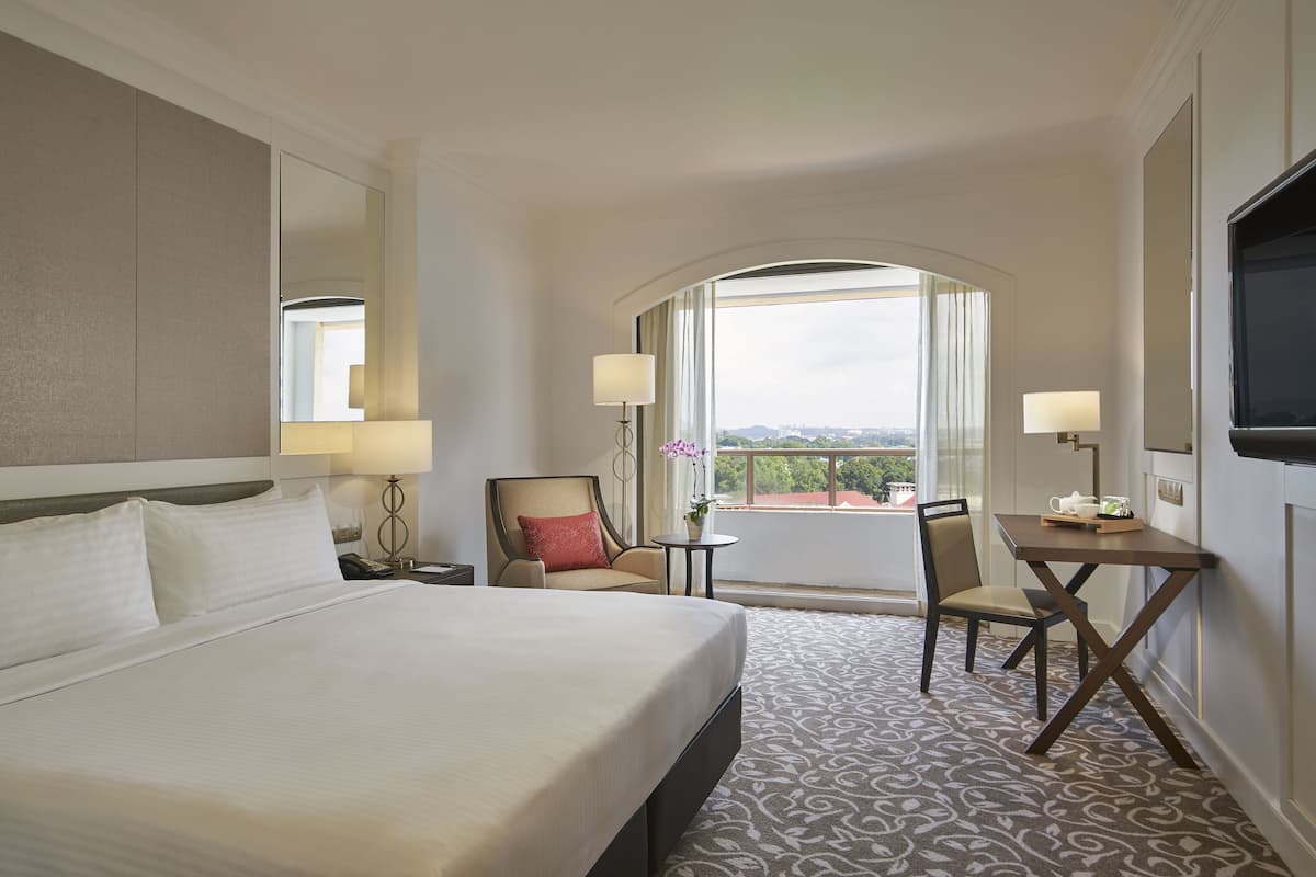 Une chambre d’hôtel avec un grand lit, un bureau avec une chaise, une petite table avec une lampe et une grande fenêtre donnant sur la ville.