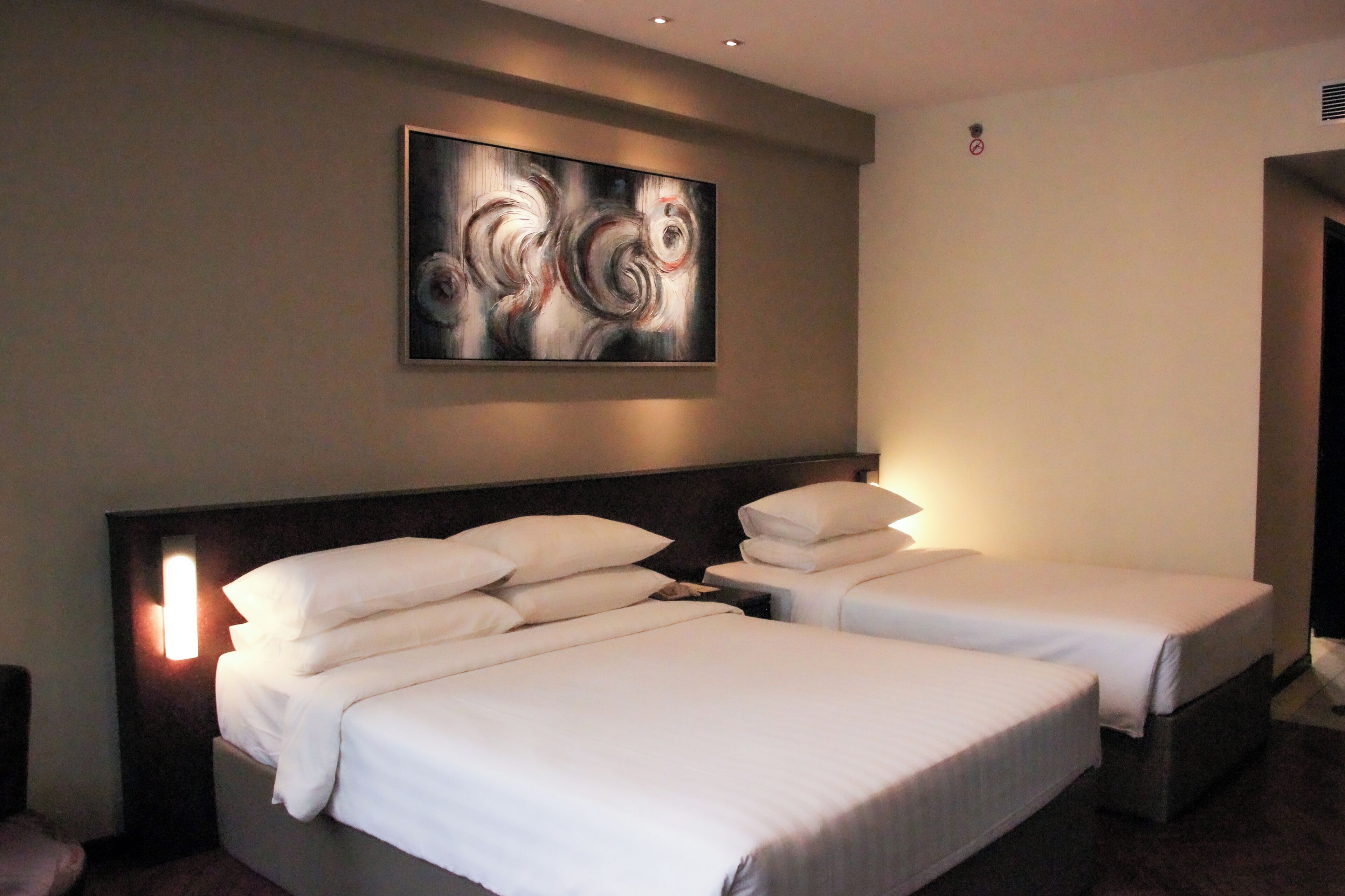 Habitación de hotel con dos camas, un cuadro abstracto grande en la pared y una mesita de noche con lámpara.