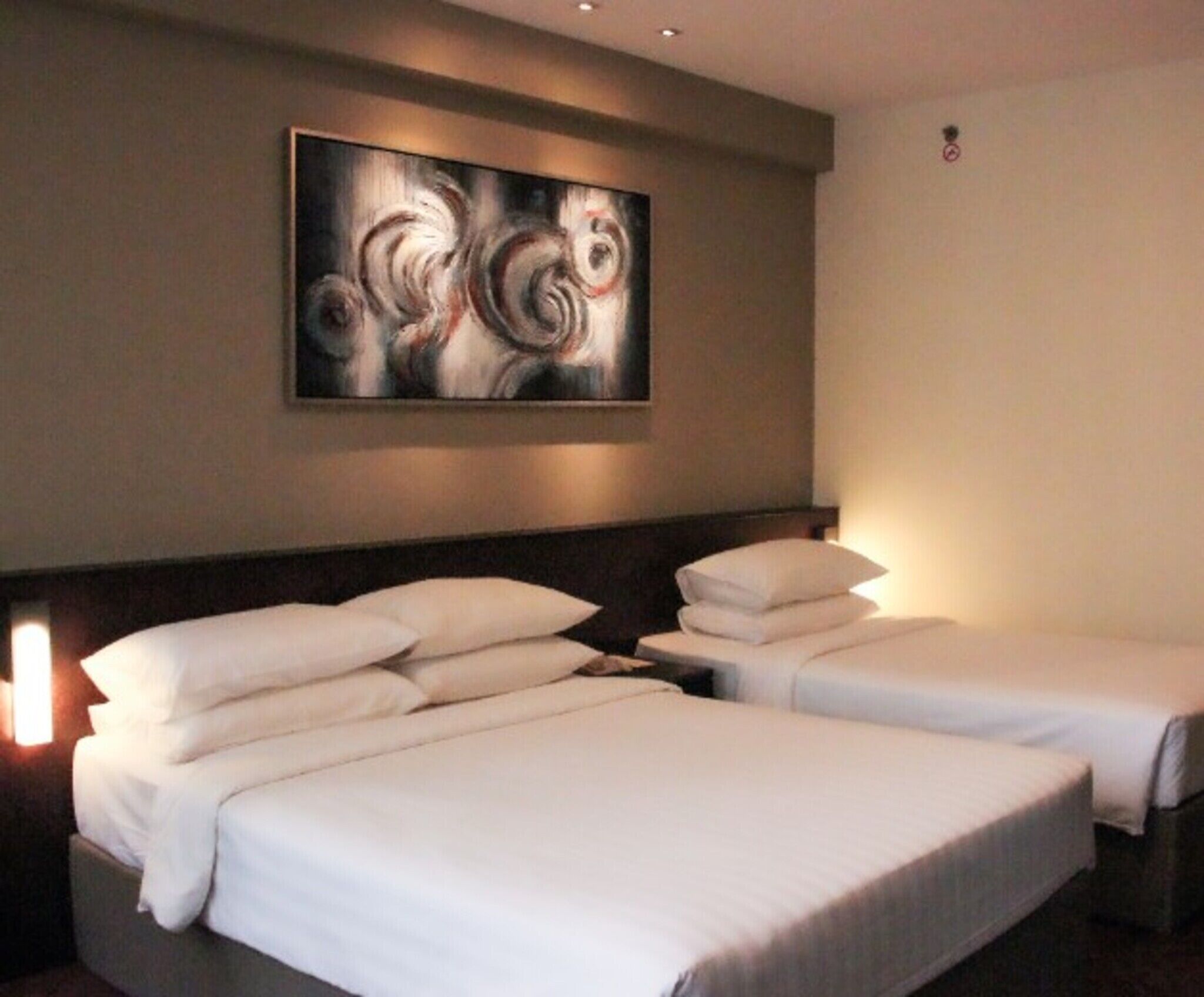 A hotel room with two beds, a large abstract painting on the wall, and a nightstand with a lamp.