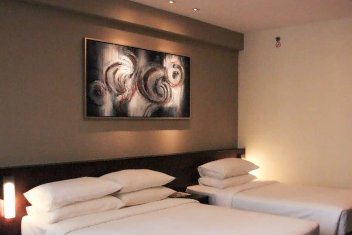 A hotel room with two beds, a large abstract painting on the wall, and a nightstand with a lamp.