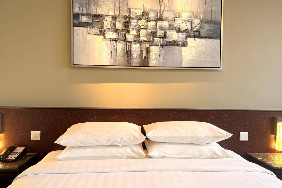 A hotel room with a large abstract painting, a neatly made bed with white linens, and bedside lamps.