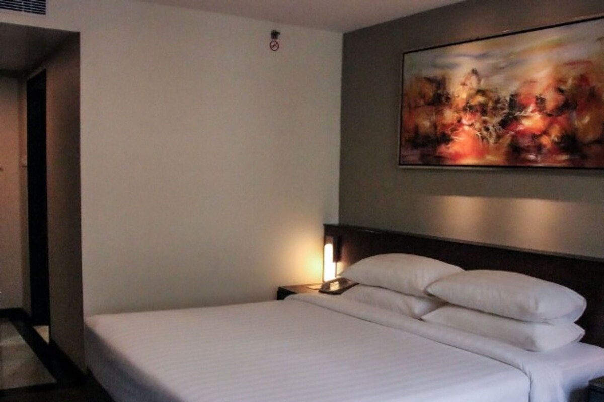 A hotel room with a bed, a nightstand, a lamp, and a painting on the wall.