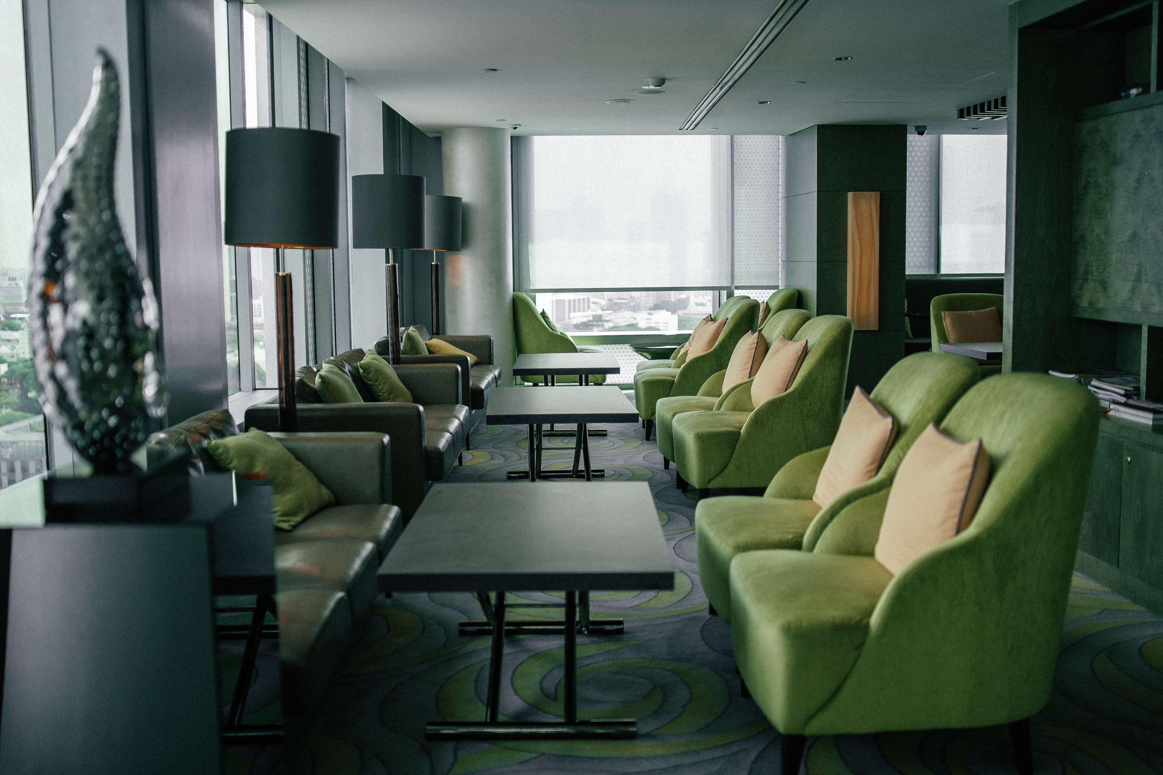 A modern hotel lobby with green seating, large windows, and a city view.